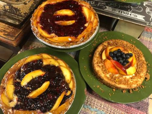 Three delicious pies: one with peach and berry topping, one with peach slices, and a cheesecake with fruit on top.