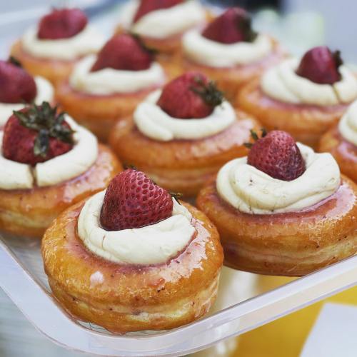 A tray of glazed pastries topped with cream and fresh strawberries.