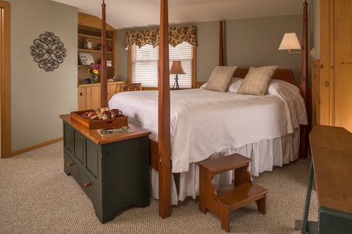 Cozy bedroom featuring a four-poster bed, decorative pillows, a wooden chest, and warm lighting.