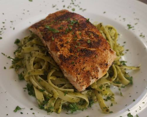 A perfectly cooked salmon fillet on a bed of pesto pasta, garnished with fresh herbs.