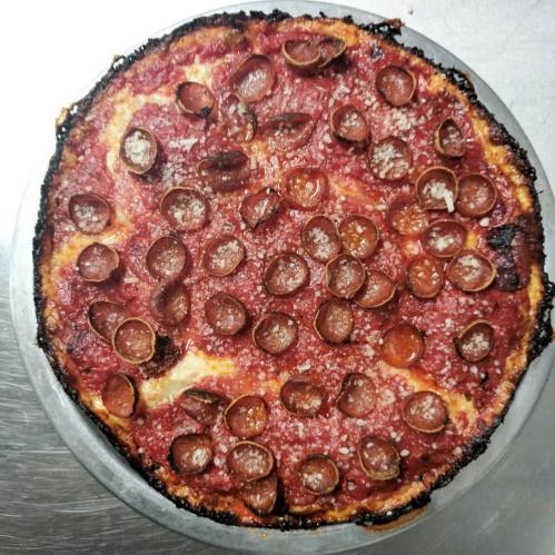 A round pizza topped with pepperoni and a slightly charred crust, placed on a metal surface.