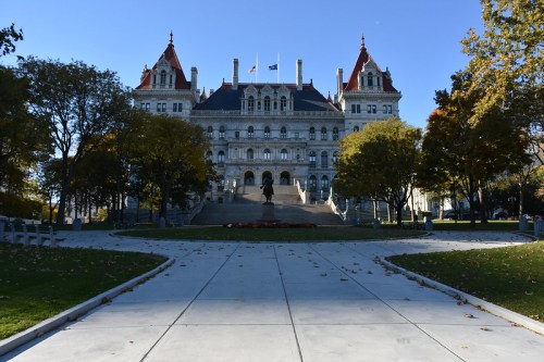 The New York State Capitol building, featuring ornate architecture and surrounded by trees in a park setting.