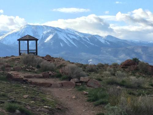 A scenic view of a gazebo on a rocky path, with snow-capped mountains and a blue sky in the background.