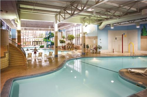 Indoor swimming pool area with a water slide, lounge chairs, and large windows letting in natural light.
