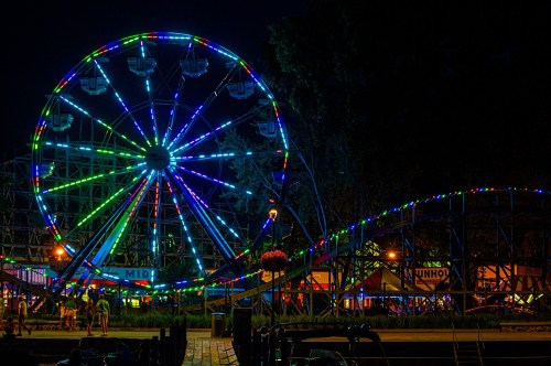 A brightly lit Ferris wheel and roller coaster at night, surrounded by colorful lights and a festive atmosphere.