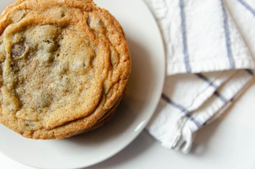 A stack of freshly baked cookies on a white plate, next to a folded striped kitchen towel.