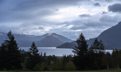A serene landscape featuring mountains, a lake, and trees under a cloudy sky.
