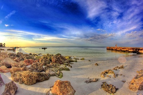 A serene beach scene with rocky shorelines, calm waters, and a colorful sky at sunset.