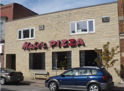 Exterior of Mabel's Pizza, featuring a stone facade and large red sign, with parked cars in front.
