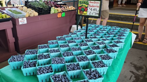 A display of fresh blueberries in green baskets at a market, with a sign showing prices.
