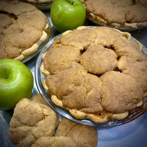 Freshly baked apple pies with golden crusts, surrounded by green apples on a silver tray.