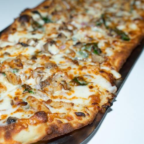 A close-up of a rectangular pizza topped with melted cheese, mushrooms, and green herbs on a metal tray.