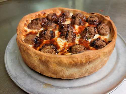 A deep-dish pizza topped with meatballs and a golden-brown crust, served on a metal tray.