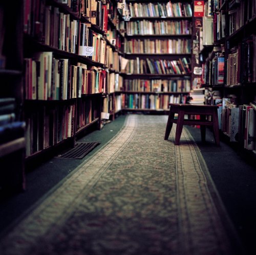 A cozy library aisle lined with bookshelves and a small table in the center, inviting quiet reading.