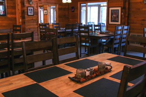 Cozy wooden dining area with tables, chairs, and a centerpiece of candles and pinecones on a table.