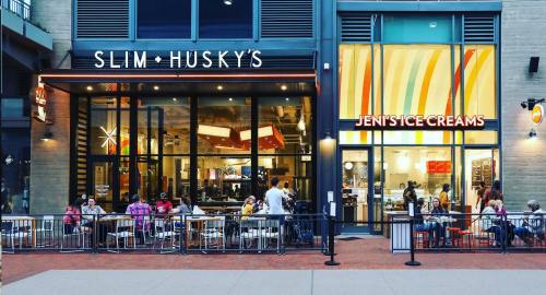 Exterior view of Slim & Husky's and Jeni's Ice Creams, with people dining outside on a lively street.