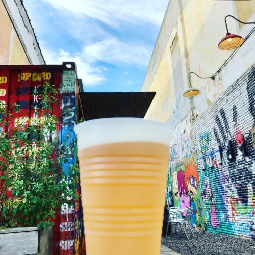 A frosty beer in a plastic cup, with a colorful graffiti wall and blue sky in the background.