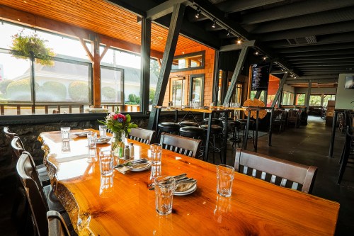 A rustic restaurant interior featuring a wooden table set with glassware and a view of the outdoor seating area.