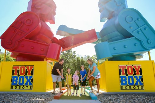 A family plays mini-golf between two large, colorful robot sculptures at Toy Box Robots.