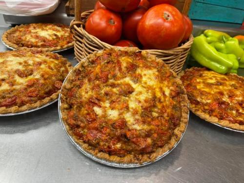 Four savory pies with a golden crust, topped with melted cheese and tomatoes, alongside fresh tomatoes and green peppers.