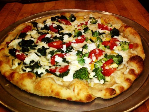 A freshly baked pizza topped with tomatoes, broccoli, spinach, and feta cheese on a golden crust.