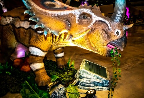 A colorful dinosaur sculpture with intricate details, surrounded by greenery and illuminated by soft lights.
