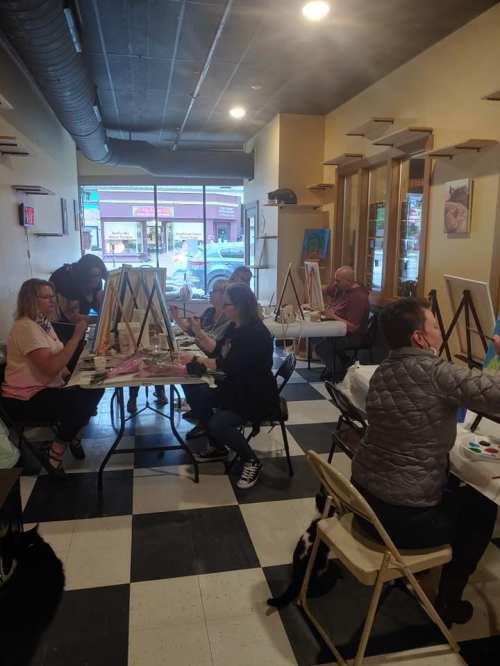 A group of people painting on easels in a bright, spacious art studio with large windows.