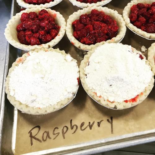 Freshly made raspberry pies on a baking tray, some topped with powdered sugar, labeled "Raspberry."
