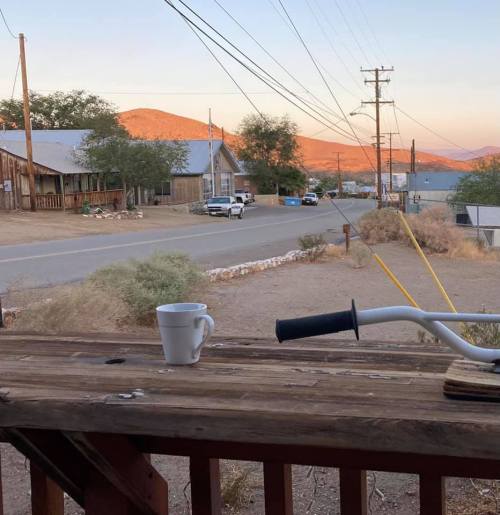 A view of a quiet street with a white mug on a wooden railing, surrounded by hills and power lines at sunset.