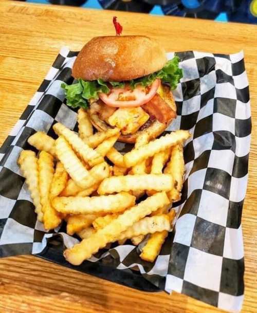 A delicious burger with lettuce, tomato, and bacon, served with a side of crispy crinkle-cut fries on a checkered plate.