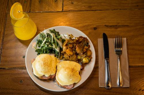 A plate of eggs Benedict with greens and a side of savory stuffing, accompanied by two glasses of orange juice.
