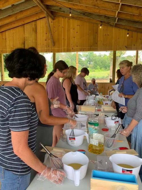 A group of people in a rustic setting, engaged in a cooking or crafting activity with various ingredients and tools.