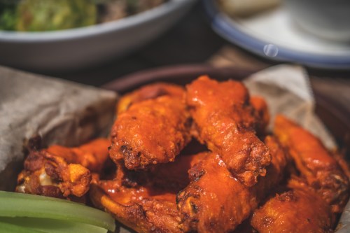 A close-up of spicy chicken wings coated in sauce, served with celery sticks on a plate.