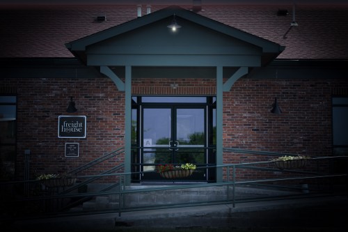 Entrance of a brick building with a sign reading "freight house," featuring a ramp and flower planters.