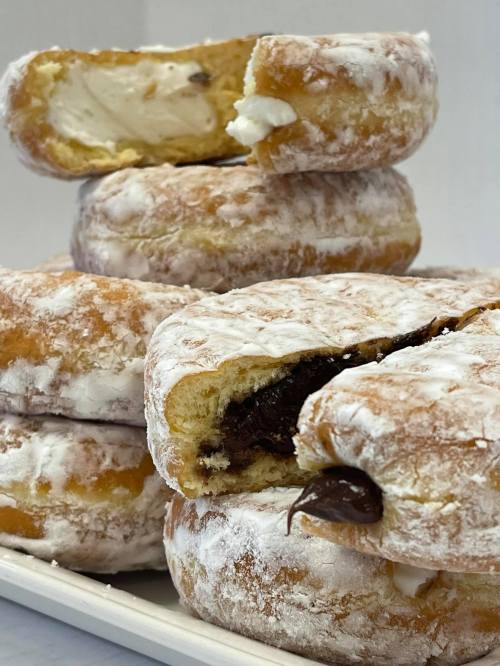 A stack of powdered sugar donuts filled with cream and chocolate, some partially bitten.