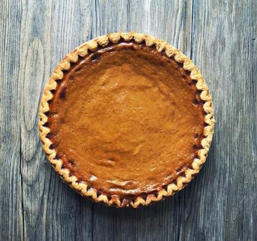 A freshly baked pumpkin pie in a golden crust on a wooden surface.
