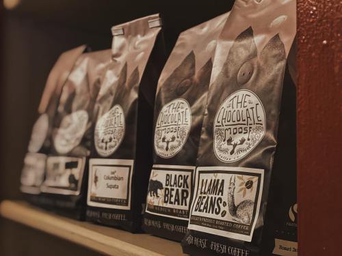 Three bags of coffee on a shelf, labeled "Colombian Supremo," "Black Bear," and "Llama Beans."