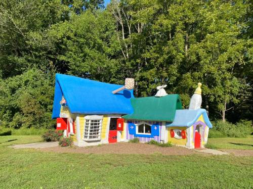 A whimsical, colorful cottage with a blue roof and vibrant walls, surrounded by greenery and a clear blue sky.