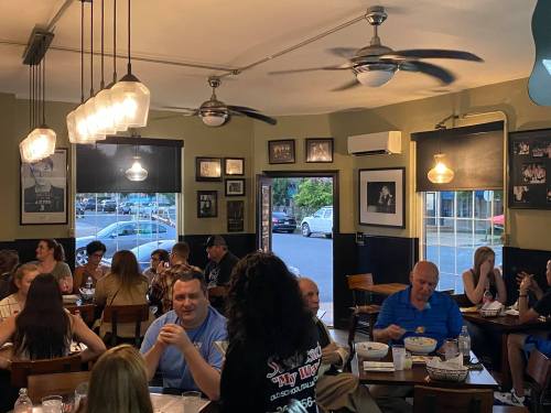 A busy restaurant scene with diners enjoying meals, chatting, and a server attending to guests. Warm, inviting atmosphere.