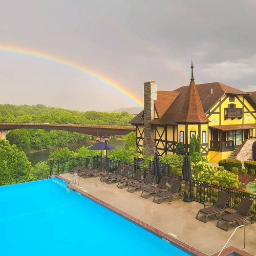 A scenic view featuring a pool, a charming house, and a rainbow over a lush landscape after a rainstorm.