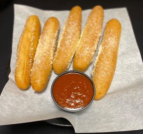 A plate of five golden breadsticks sprinkled with cheese, served with a small bowl of marinara sauce.