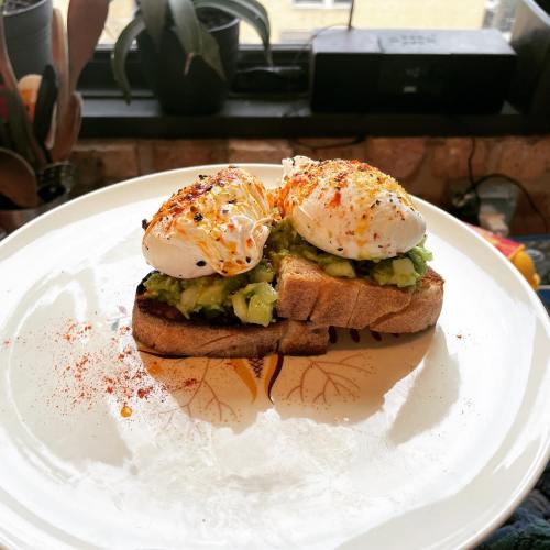 Avocado toast topped with poached eggs and spices, served on a decorative plate.