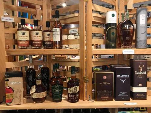 A wooden shelf displaying various whiskey bottles, including brands like Foundry, Dalmore, and Glenfiddich.