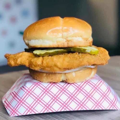 A crispy chicken sandwich with pickles and mayonnaise, served on a toasted bun, resting on a checkered paper.