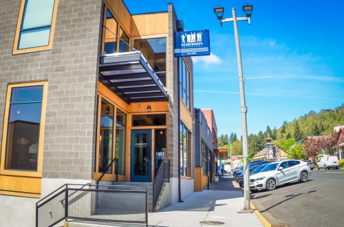 A modern building with wooden accents and large windows, featuring a sign for "Everybody's" and a clear blue sky.