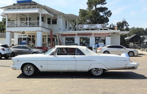 A classic white convertible parked in front of a vintage store with a sign reading "Cooper's Grocery Store."