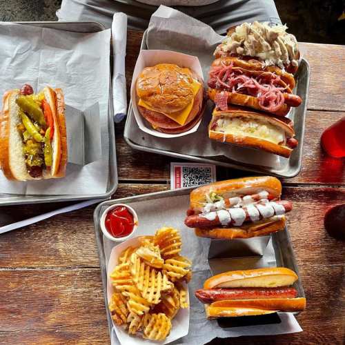 A table with trays of hot dogs, a cheeseburger, and waffle fries, accompanied by condiments and a QR code.