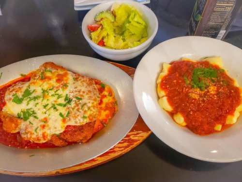 A plate of chicken parmesan with melted cheese and marinara sauce, alongside gnocchi in tomato sauce and a side salad.