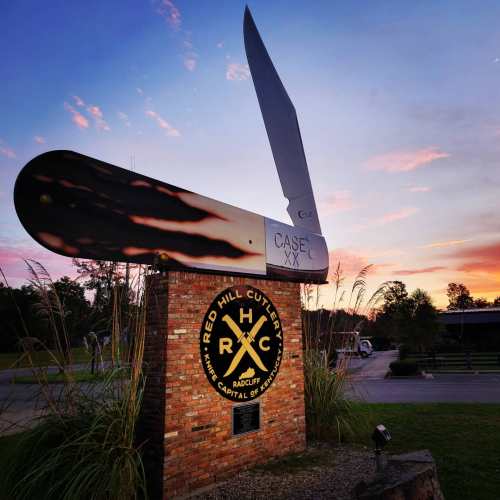 A large knife sculpture at sunset, featuring the text "Red Hill Cutlery" and "Case XX" on a brick base.