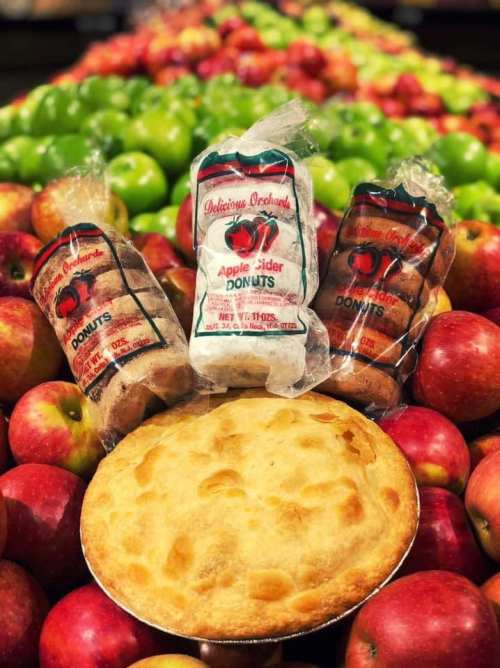 A display of fresh apples with apple cider donuts and a pie in the center, showcasing autumn treats.